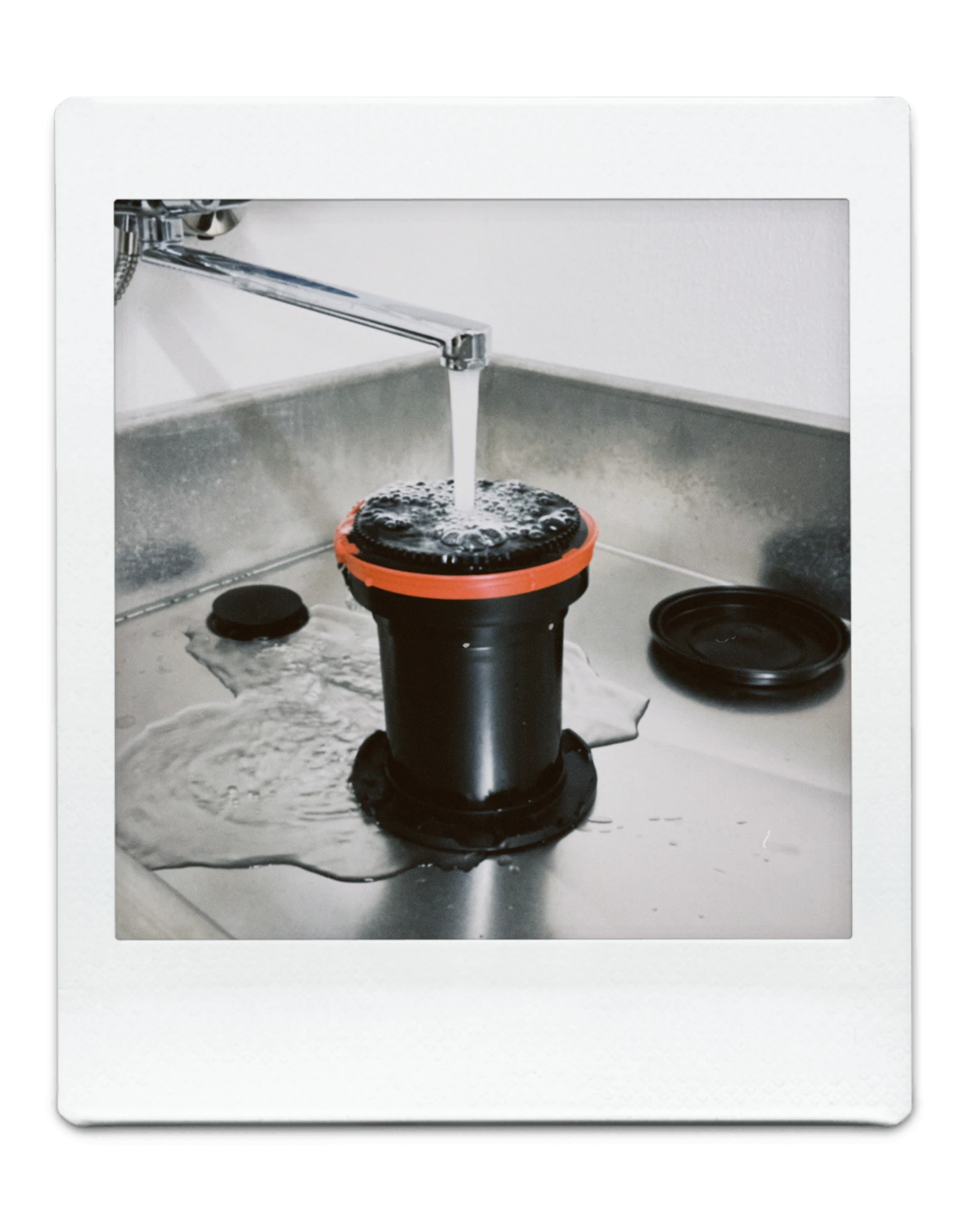 Polaroidfoto laborist: ilmutustank terasest valamus kraani all, film loputub